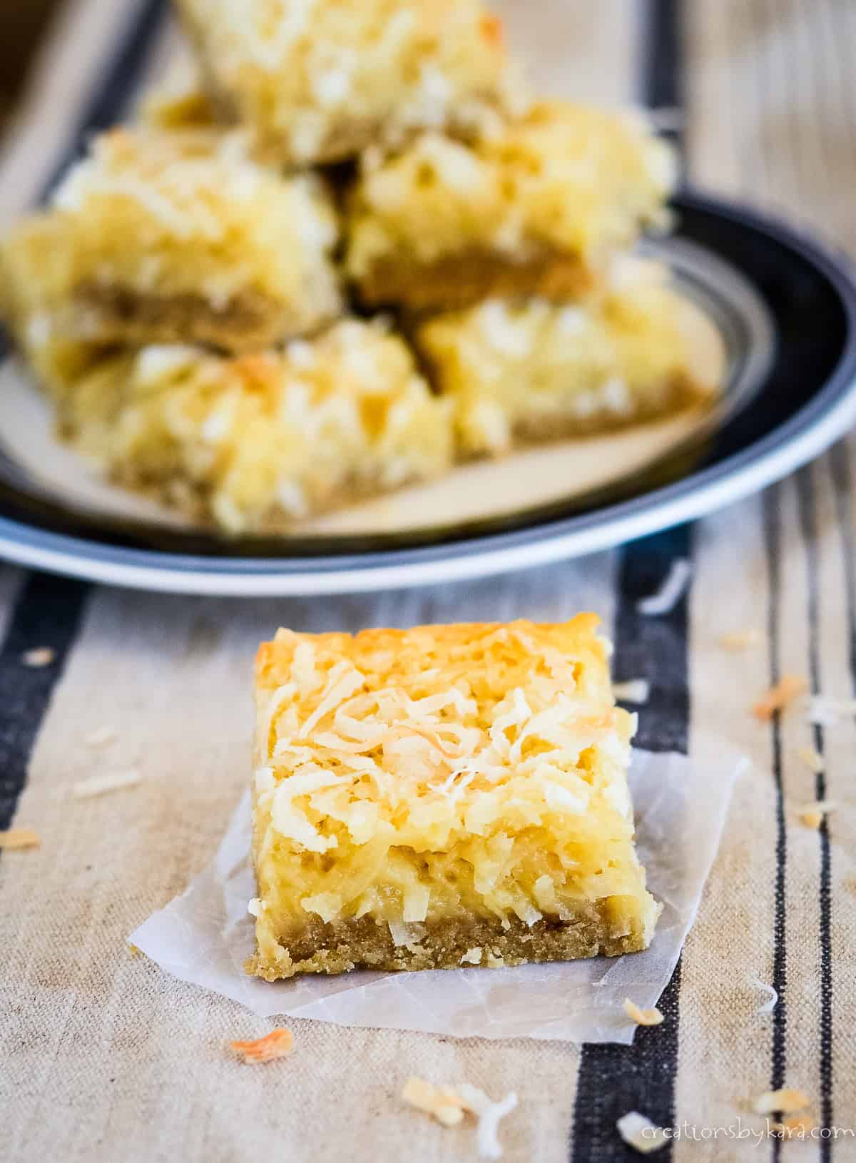 coconut bar on waxed paper with a plate of coconut bars in the background